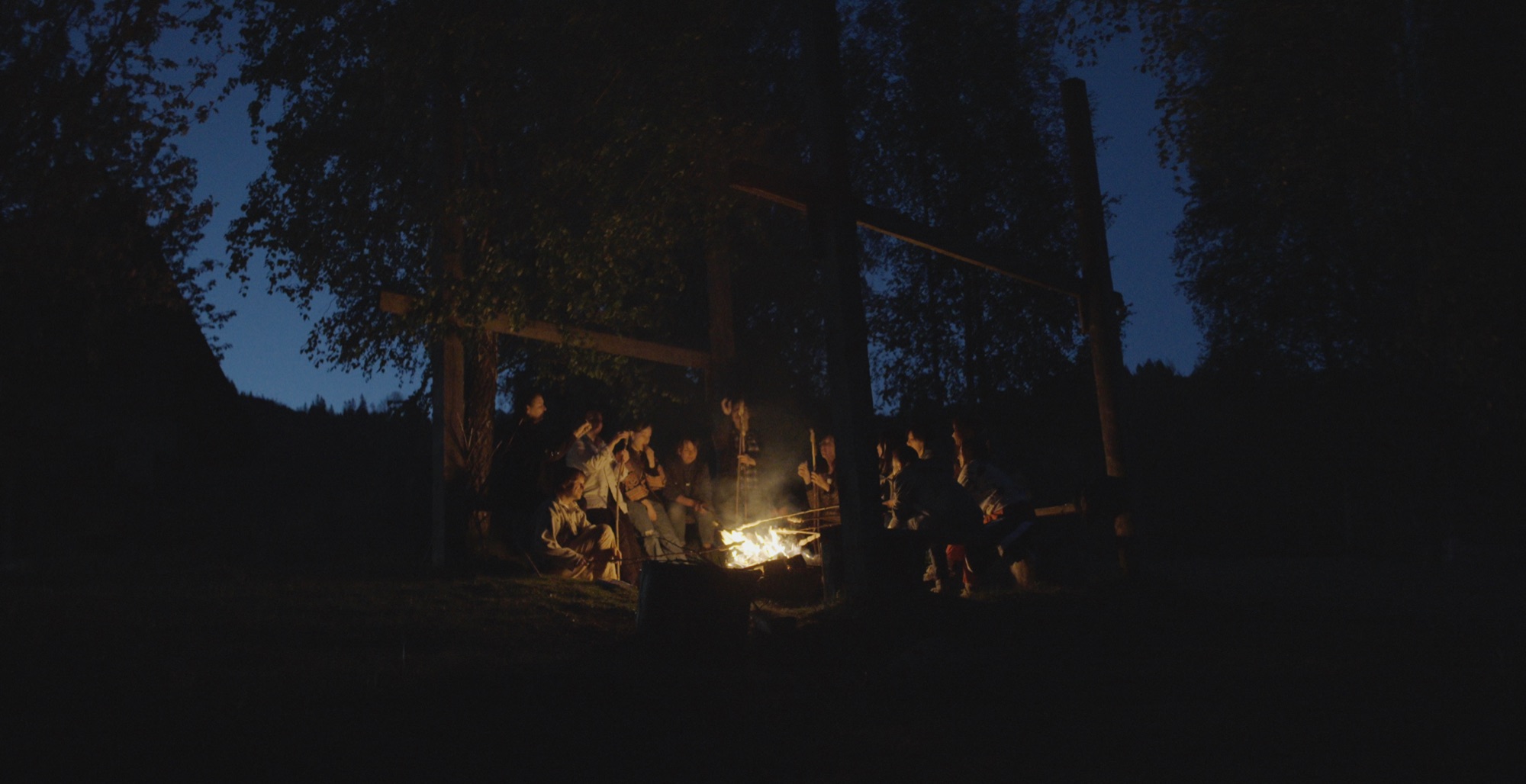 Gruppe sitzt nachts im Wald um ein Lagerfeuer